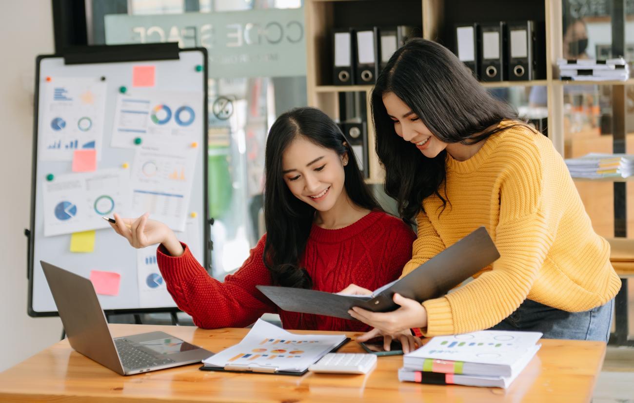 Duas mulheres colaborando em um laptop em um escritório, focadas em uma tarefa conjunta.